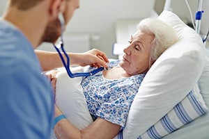 yolo-300x200-85-1 Medical professional with stethoscope on elderly woman in bed.