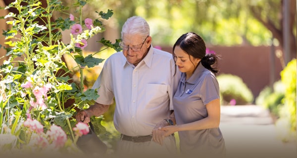 An elderly man walking around outside with a caretaker